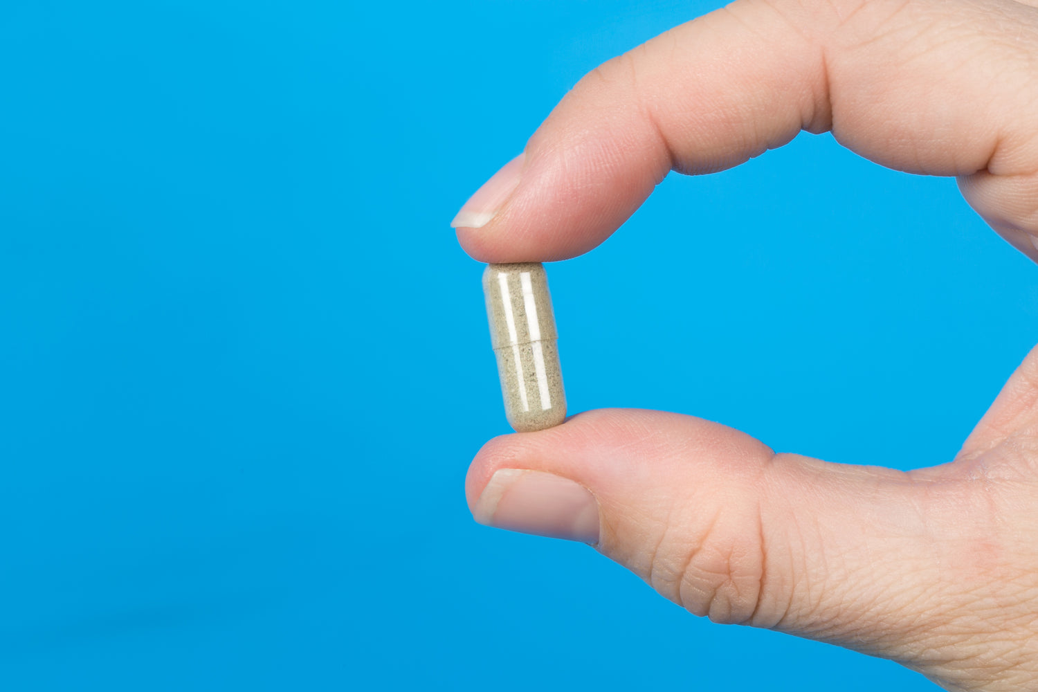 Plant-based supplement capsule held between fingers, representing purity and natural health support