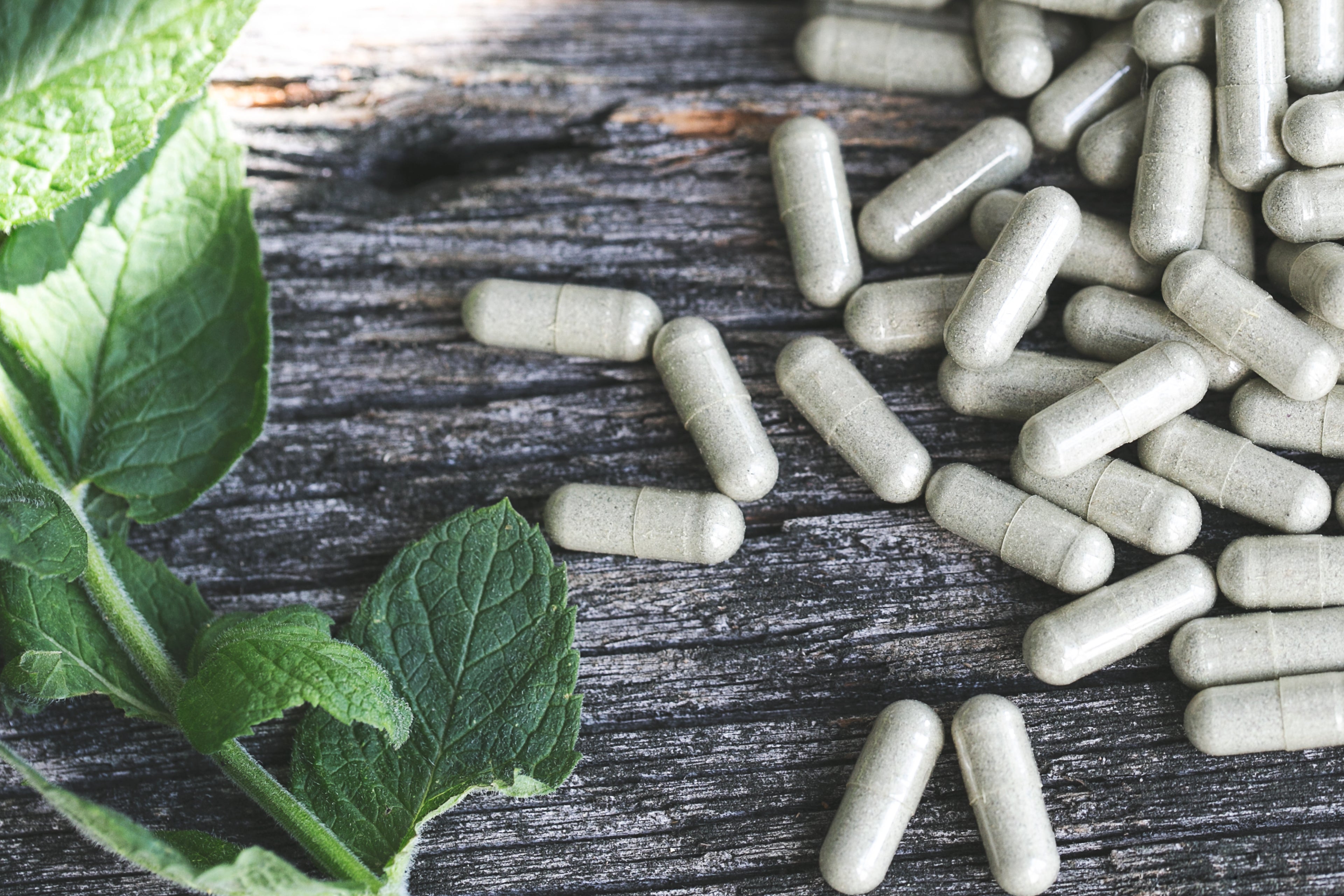 Clean herbal supplement capsules with mint leaf on rustic wood, emphasizing nature-inspired wellness and freshness